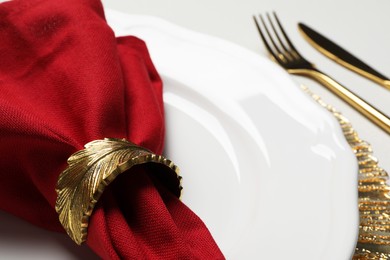 Photo of Plate with red fabric napkin, decorative ring and cutlery on white table, closeup