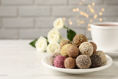 Delicious vegan candy balls on white wooden table against blurred lights, space for text