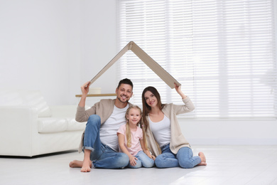 Happy family sitting under cardboard roof at home. Insurance concept
