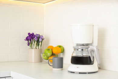 Photo of Coffeemaker, cup, fruits and flowers on counter in kitchen