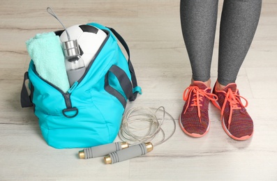 Young woman in sportswear and bag with gym equipment indoors