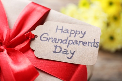 Beautiful gift box and tag with phrase Happy Grandparents Day on table, closeup