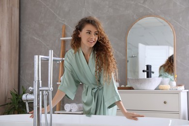 Beautiful woman in green silk robe near bathtub at home