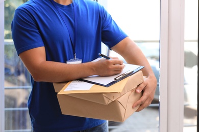 Young courier with parcels and clipboard on doorstep, closeup. Delivery service