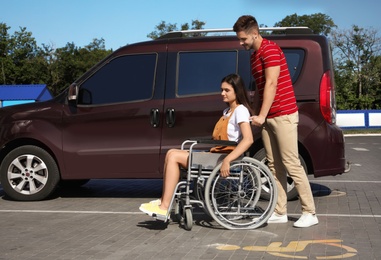 Young man with woman in wheelchair near van on car parking