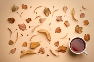 Flat lay composition with cup of hot drink and autumn leaves on beige background. Cozy atmosphere