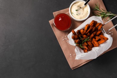 Frying basket with sweet potato fries and sauces on black table, top view. Space for text