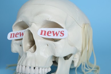 Information and media warfare concept. Human skull with noodles and words News in eye sockets on light blue background, closeup