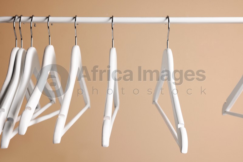Photo of White clothes hangers on metal rail against beige background