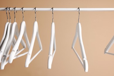 White clothes hangers on metal rail against beige background