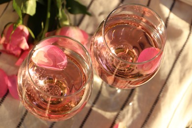 Photo of Glasses of delicious rose wine with petals and flowers on white picnic blanket, closeup
