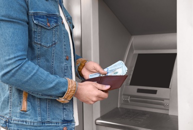 Young man with money near cash machine outdoors, closeup
