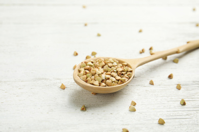 Uncooked green buckwheat grains in spoon on white wooden table