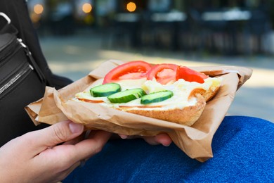 Woman holding tasty sandwich with vegetables outdoors, closeup. Street food