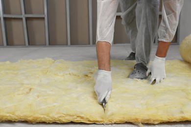 Photo of Worker cutting insulation material indoors, closeup. Space for text