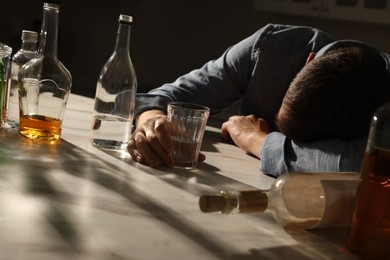 Addicted man with alcoholic drink sleeping at table indoors