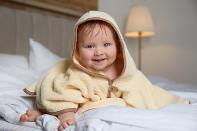 Cute little baby in yellow hooded towel on bed after bath