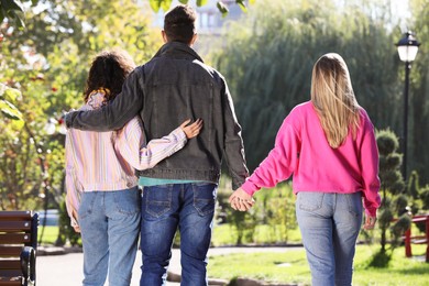 Man holding hands with another woman while hugging his girlfriend during walk in park, back view. Love triangle