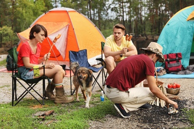 Photo of Young people having lunch with sausages near camping tents outdoors