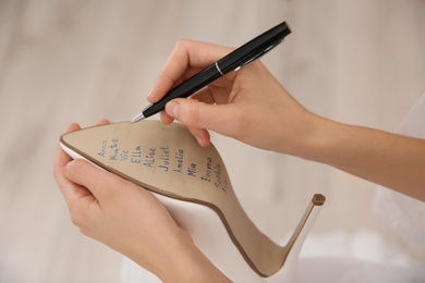 Young bride writing her single friends names on shoe indoors, closeup. Wedding superstition