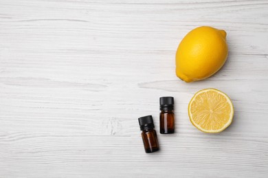 Bottles of citrus essential oil and fresh lemons on white wooden table, flat lay. Space for text