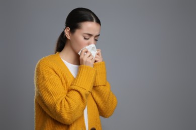Young woman blowing nose in tissue on grey background, space for text. Cold symptoms