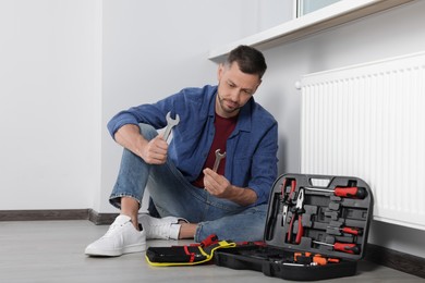 Man choosing wrench near box with tools indoors