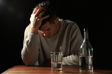 Addicted man with alcoholic drink at wooden table against black background