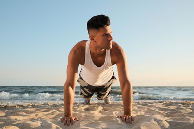 Sporty man doing plank on sandy beach