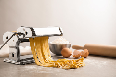 Pasta maker machine with dough on grey table. Space for text