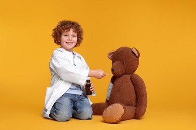 Photo of Little boy playing doctor with toy bear on yellow background