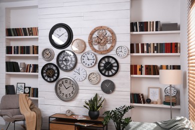Stylish room interior with rocking chair, beautiful houseplants and collection of different clocks on white wall