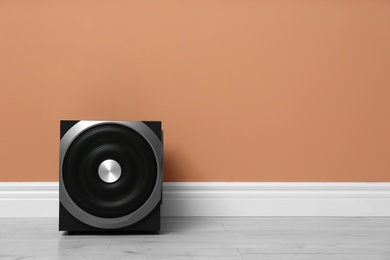 Modern powerful subwoofer on floor near orange wall, space for text. Audio speaker system