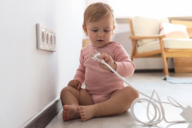 Cute baby playing with plug at home. Dangerous situation