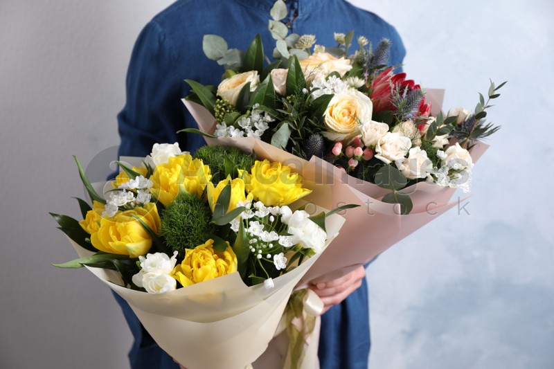 Woman with bouquets of beautiful flowers on light blue background, closeup