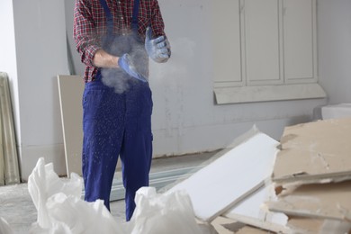 Construction worker shaking off dust from hands in room prepared for renovation, closeup