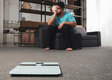 Depressed overweight man looking at scales in living room