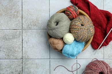 Photo of Soft woolen yarns, knitting and needles on grey tiled background, flat lay. Space for text