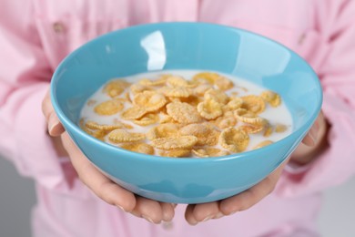 Woman holding bowl of crispy corn flakes with milk, closeup