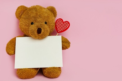 Cute teddy bear with red heart and blank card on pink background, space for text. Valentine's day celebration