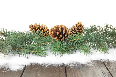 Christmas tree branches with pine cones and snow on table against white background