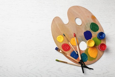 Wooden palette with colorful paints and brushes on light background, top view