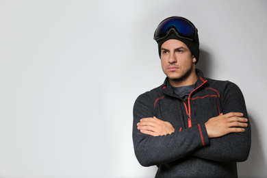 Man wearing fleece jacket and goggles on light grey background, space for text. Winter sport clothes