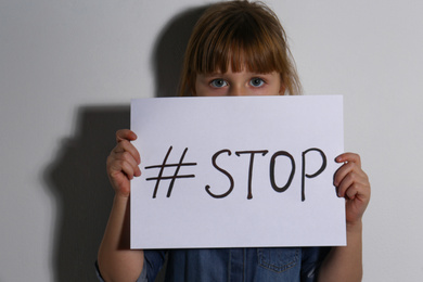 Abused little girl with hashtag STOP near white wall. Domestic violence concept