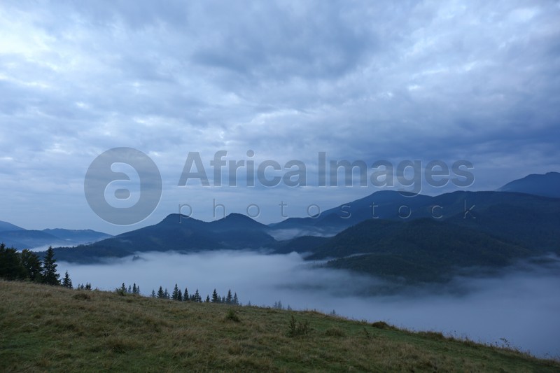Photo of Picturesque view of mountains covered with fog under cloudy sky