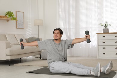 Overweight man doing exercise with dumbbells on mat at home