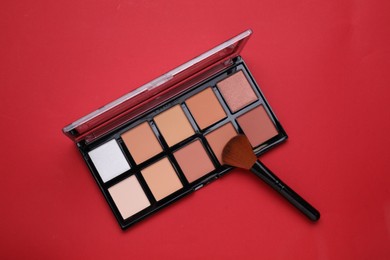 Photo of Colorful contouring palette with brush on red background, top view. Professional cosmetic product