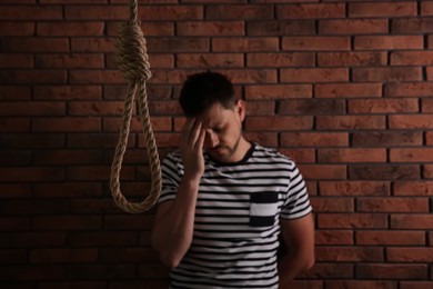 Depressed man near brick wall, focus on rope noose