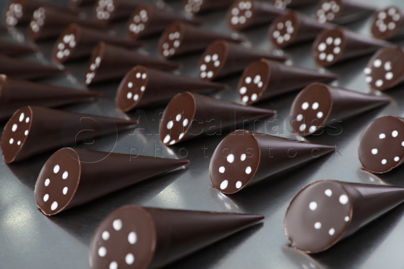 Photo of Many tasty chocolate candies on metal surface, closeup. Production line