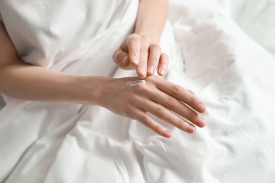 Woman applying hand cream in bed, closeup